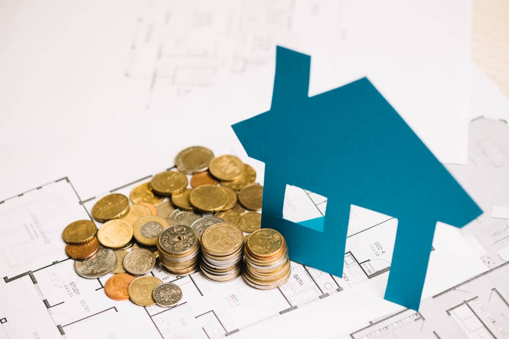 Coins and a paper house cutout resting on house blueprints
