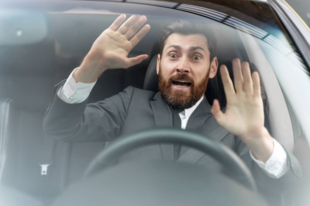 Startled man driving with hands raised near the windshield